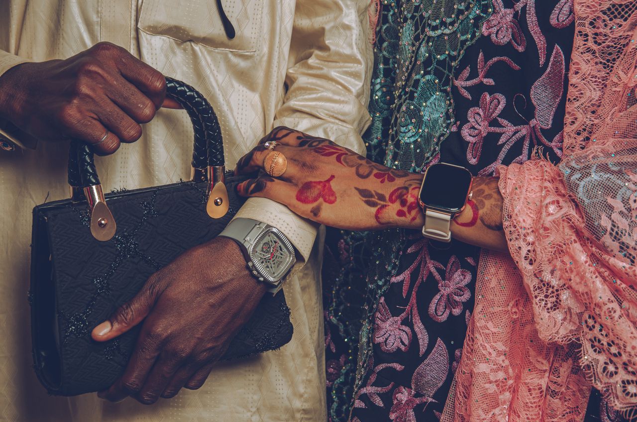 Home Closeup of hands with watches and henna, dressed in traditional attire, holding a purse.